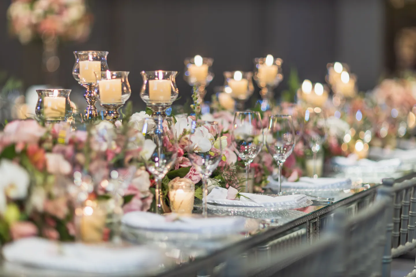 A reception table with glass candleholders, pink and white flowers, and place settings
